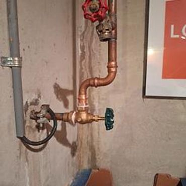 Copper water pipes with red and blue valves against a concrete wall.