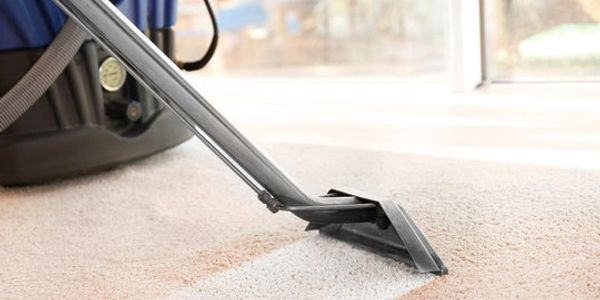 Carpet cleaning machine in action on beige carpet near a window.