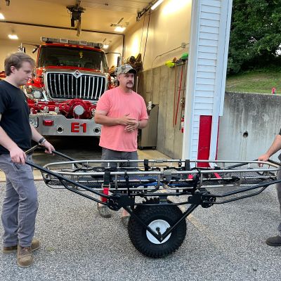 Two men moving a stretcher near a fire truck inside a fire station.