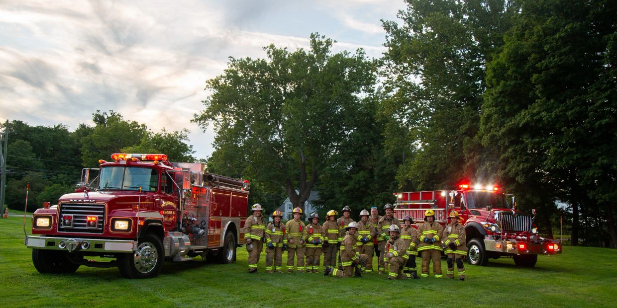 Firefighters posing with fire trucks on grass.
