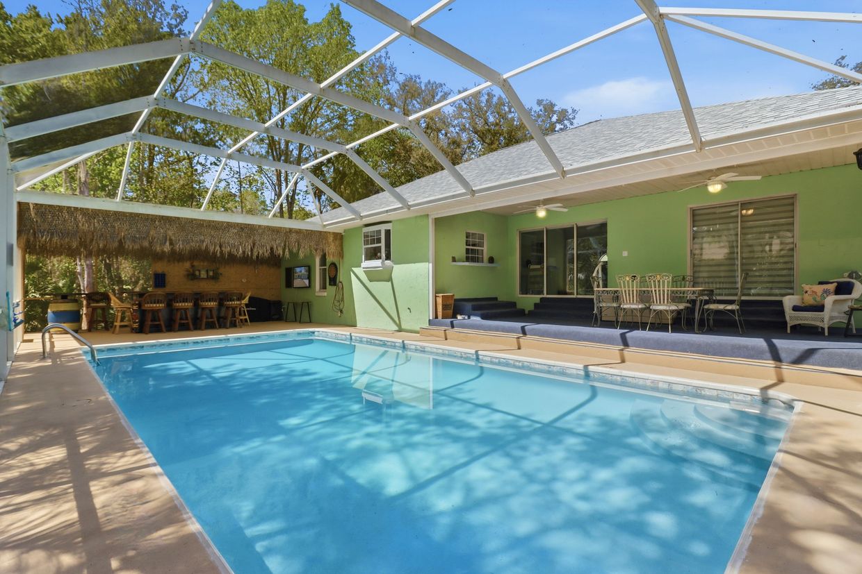 Backyard pool area with covered patio and tiki hut.