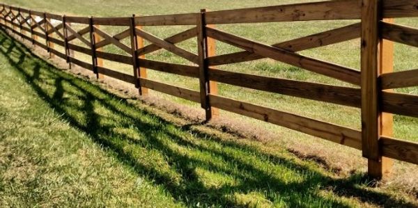 Long wooden fence casting shadows on green grass.