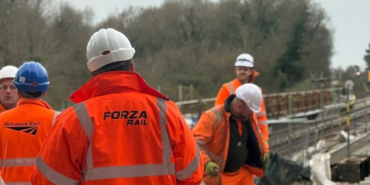 Railway workers in high-visibility jackets and hard hats on a track construction site.