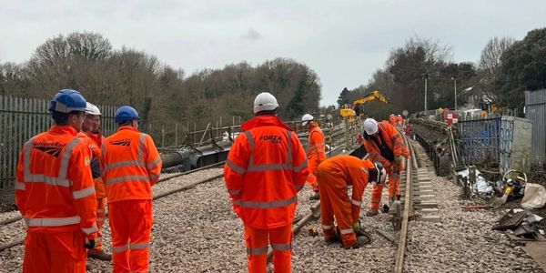 Workers in orange safety gear repairing railway tracks outdoors.