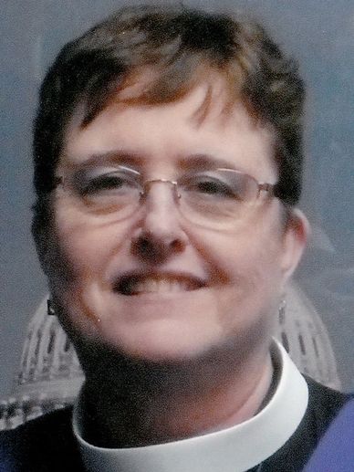 A smiling person wearing glasses and a clerical collar.