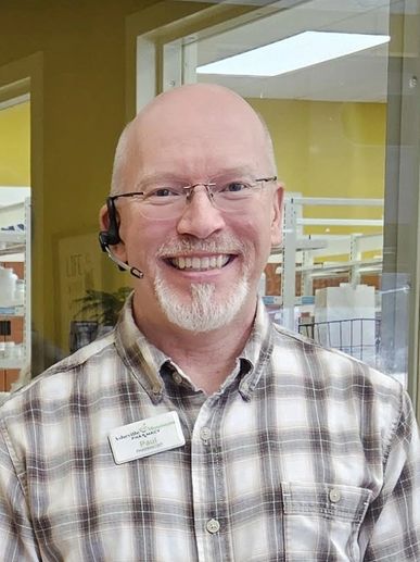 Smiling man with glasses and headset in a plaid shirt at work.