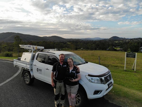 Photograph of business owners standing in front of ute with grassy area & mountains in background