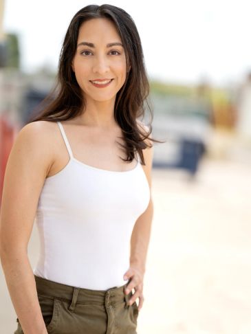Young woman with long dark hair smiling in a white tank top.