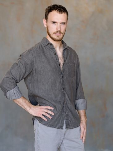 A confident man with a beard wearing a gray shirt.