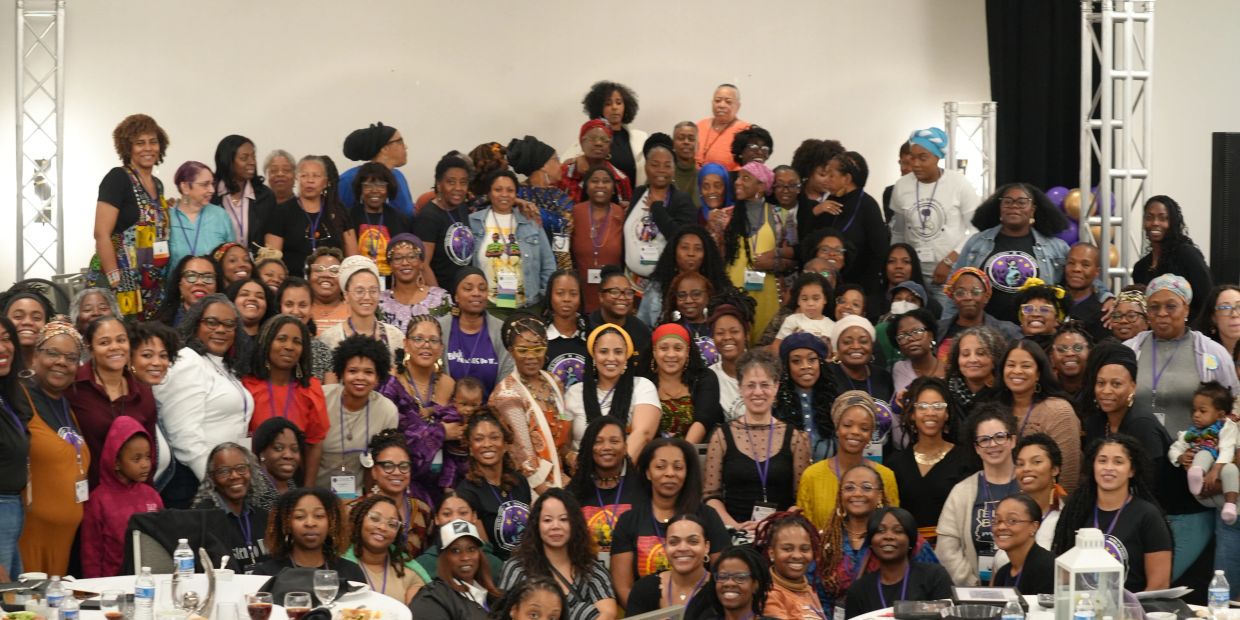 Large group of diverse women gathered indoors, smiling.