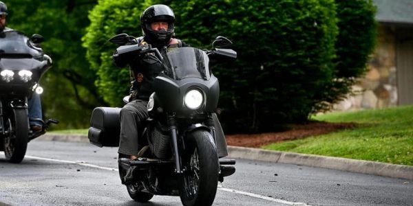 Motorcyclist riding on a street with greenery in the background.