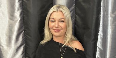 Smiling woman with blonde hair in front of black and gray curtains.