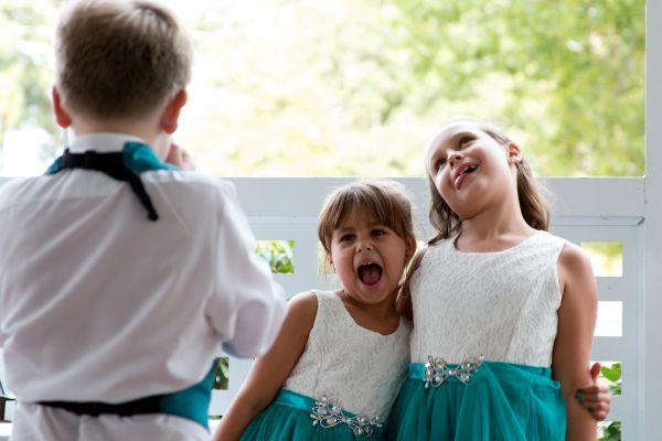 Two girls in white and teal dresses playfully posing while a boy faces them.