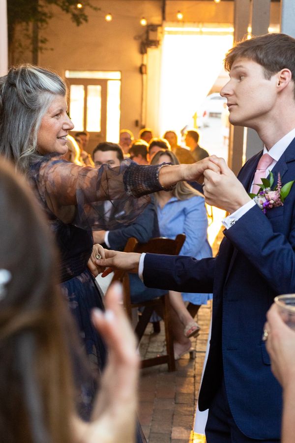 A joyful middle-aged woman and a young man in a suit dance together at a lively event.