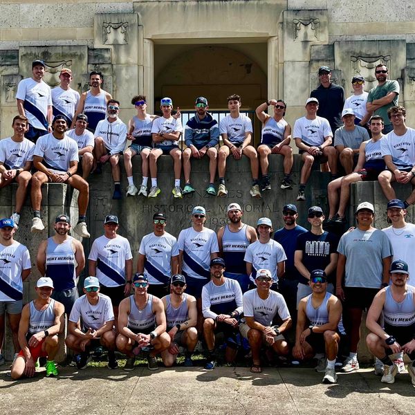 Large rowing team in uniform posing outdoors on stone steps.