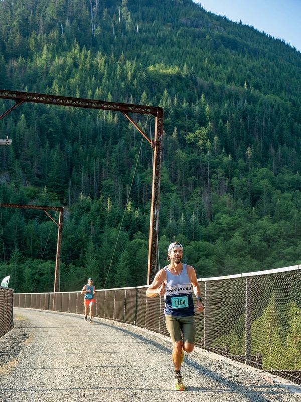 Two men running a race on a mountain trail bridge on a sunny day.