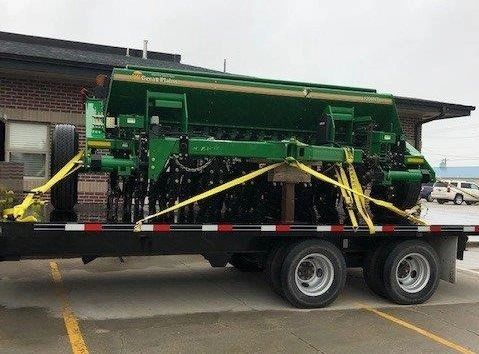 Green agricultural machinery secured on a flatbed trailer.