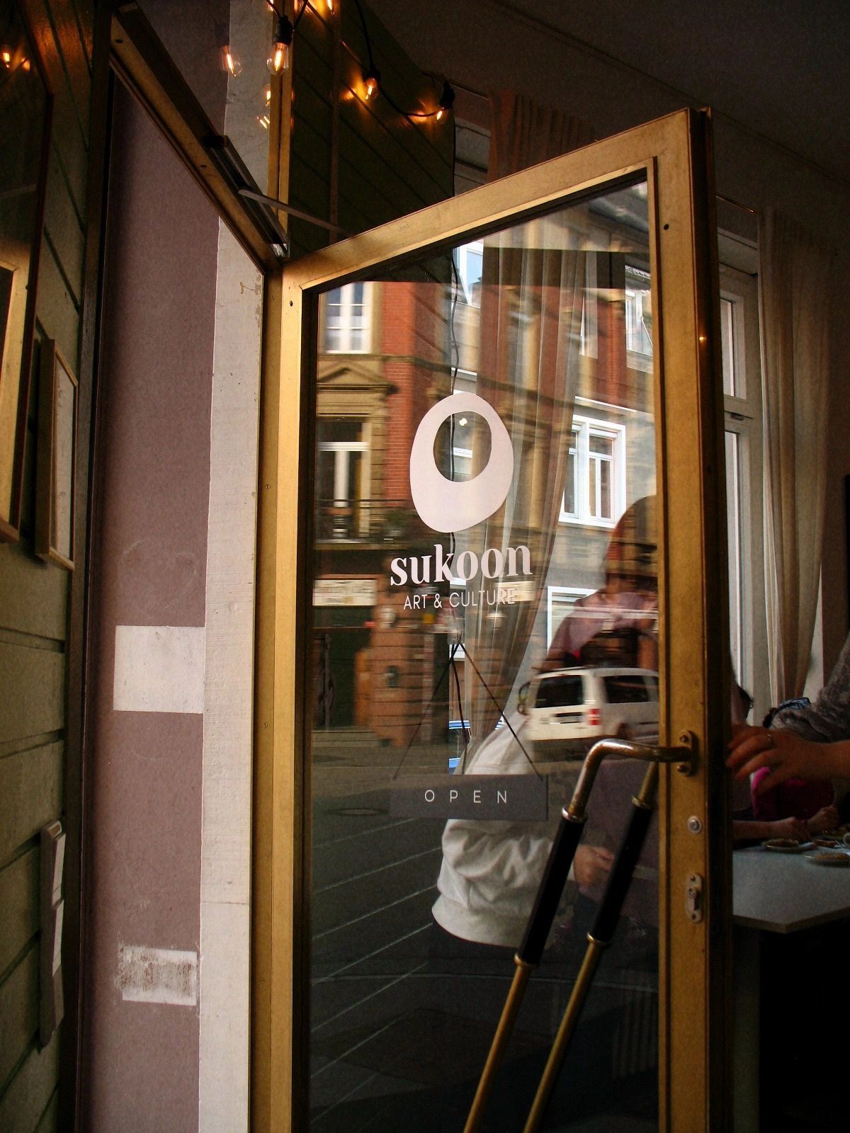 Eingangstür eines Ortes namens Sukoon Art &amp; Culture mit Spiegelung einer Straße.