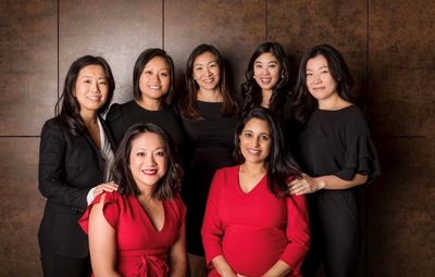Group of seven professionally dressed women posing together.