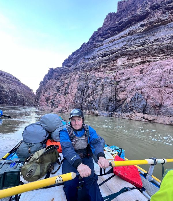 Man rowing a raft through a rocky canyon river with packed gear.