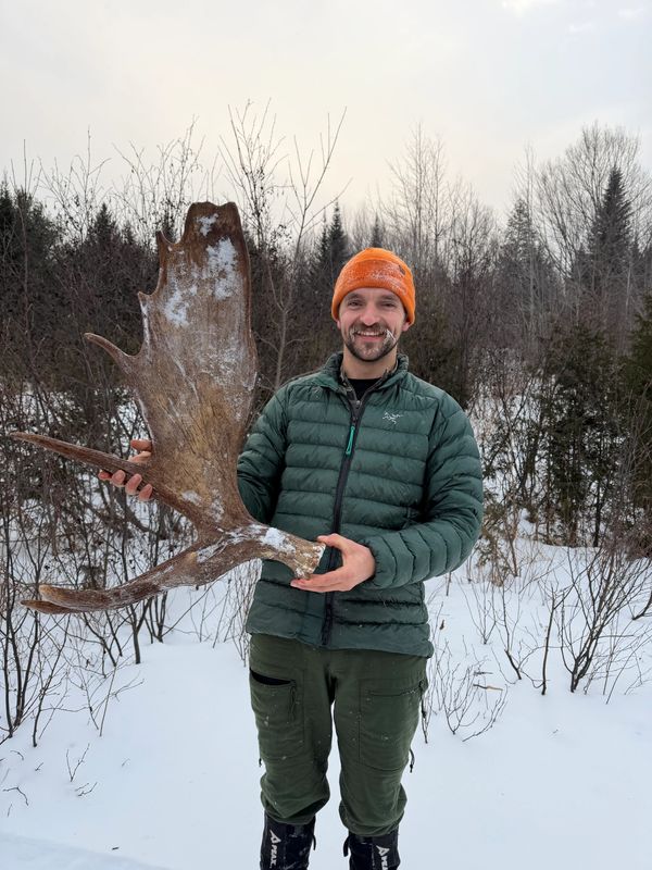 Man in winter gear holding a large moose antler outdoors.