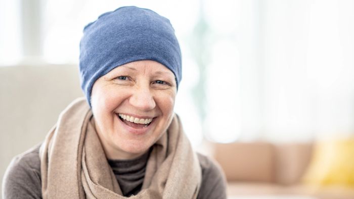 Smiling woman wearing a blue headscarf and beige scarf indoors.