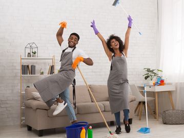 Happy couple dancing while cleaning their living room together.