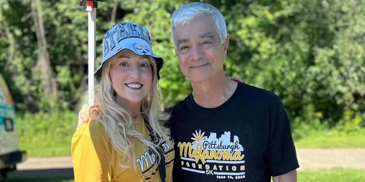 Two people smiling outdoors in matching event shirts.