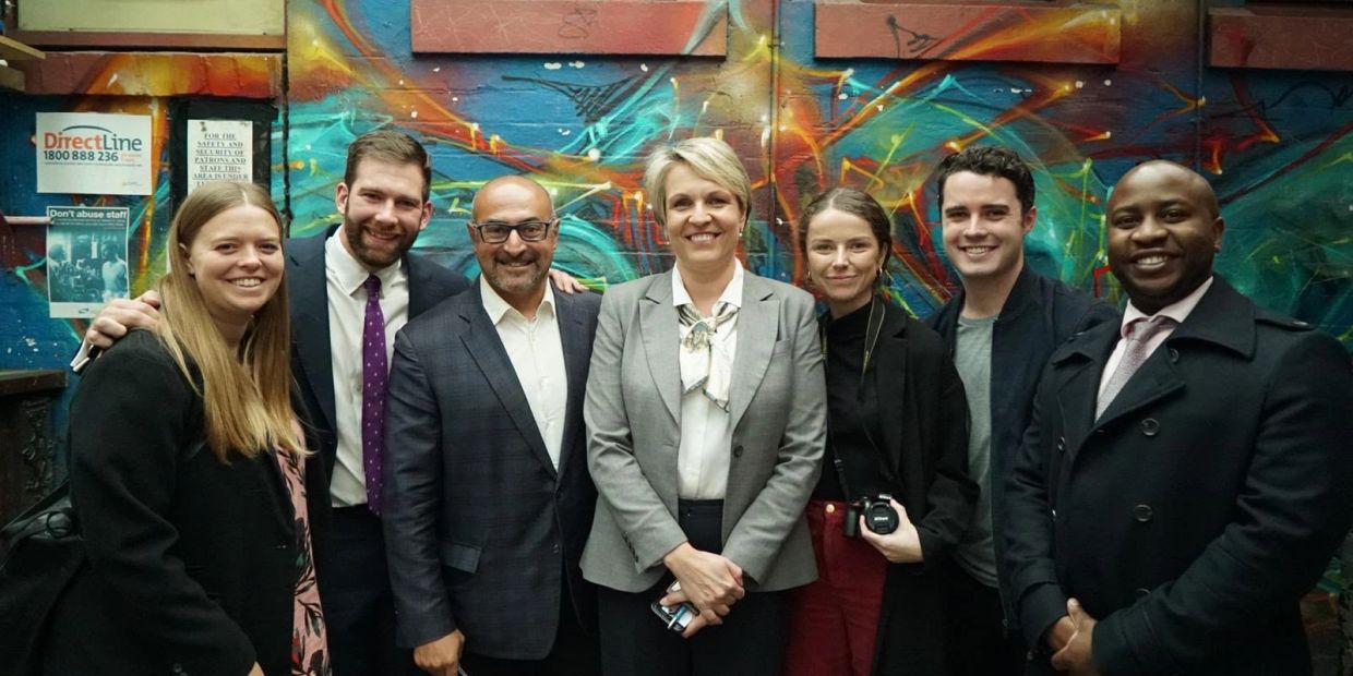 Group of seven people smiling in front of a colorful graffiti wall.