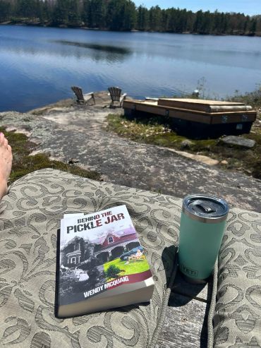 Book and drink by the lakeside with chairs and a dock in the background.