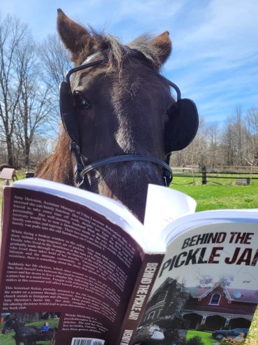A horse wearing blinders is reading a book titled 'Behind the Pickle Jar'.