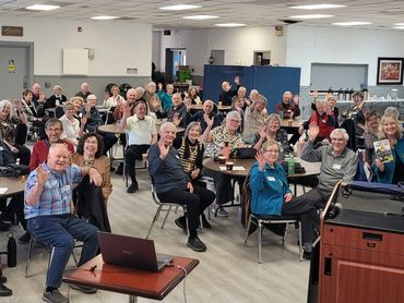 A large group of smiling seniors waving in a community room.