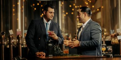 Two men in suits having a conversation at a bar with drinks.