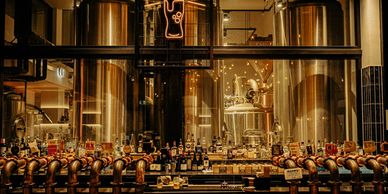 Interior of a brewery with large tanks and a bar with various taps and bottles.