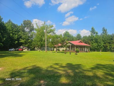 Country house with red roof and lush green lawn under a blue sky.