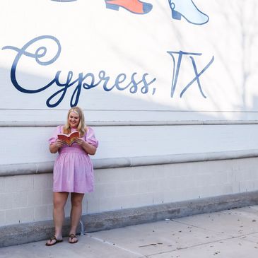 Woman in a pink dress reading by a Cypress, TX mural.