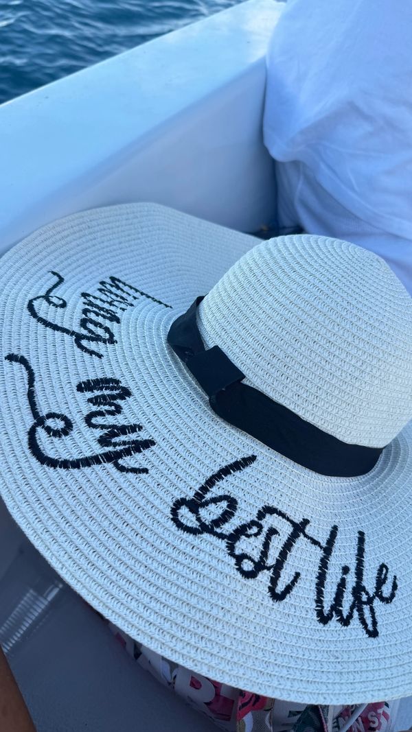 A white sun hat with a black ribbon and cursive writing on the brim.