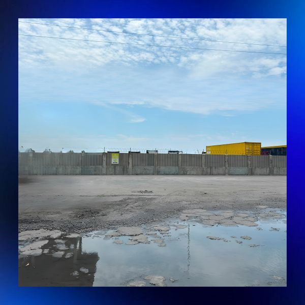 Empty industrial area with containers and puddles under cloudy sky.