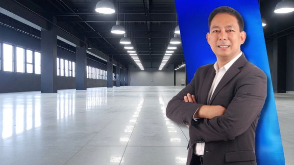 Confident businessman posing in an empty industrial warehouse with a modern blue backdrop.