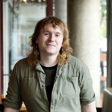 Person with curly hair and snake-shaped earrings smiling indoors.