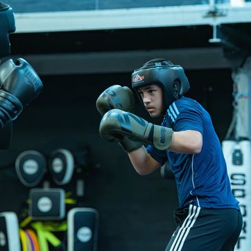 Two men sparring in boxing gear with a coach observing.