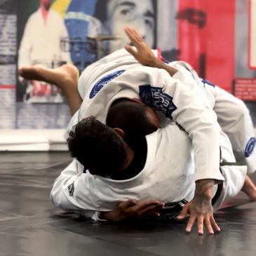 Two martial artists in white gis grappling on a mat during Brazilian Jiu-Jitsu training.