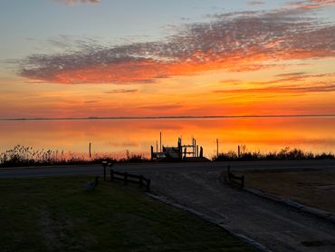 Vibrant sunset over calm water with silhouetted dock and plants.