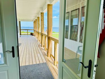 Open door leading to a wooden porch with a scenic water view.