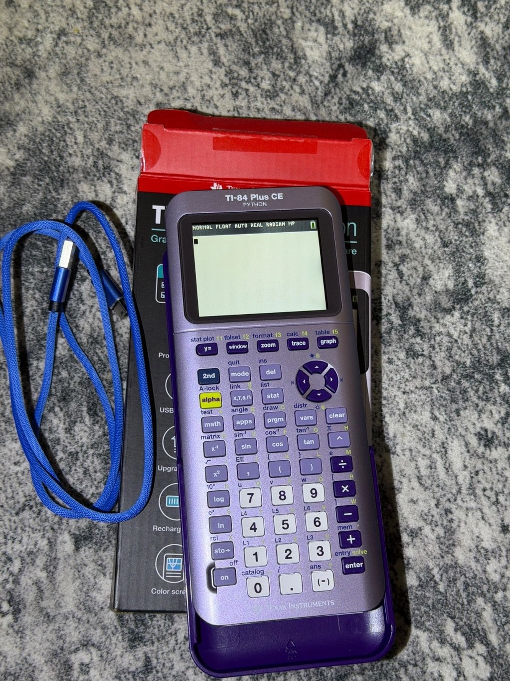 TI-84 Plus CE Python graphing calculator with blue charging cable on a gray surface.