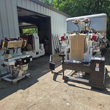 Industrial machines positioned outside a metal building on a sunny day.