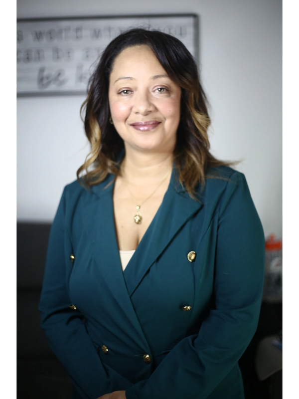 Confident woman, Tara Grenier with curled hair in teal blazer smiling. The color close to the safety green for Injury Prevention.