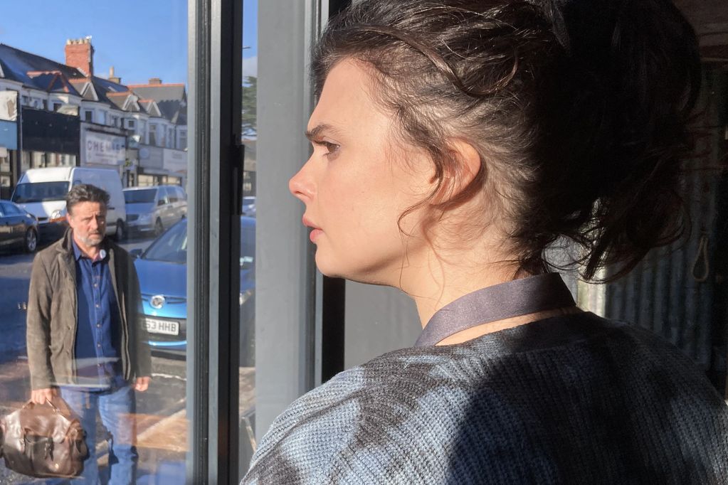 Woman looking out a window while a man stands outside with a bag.