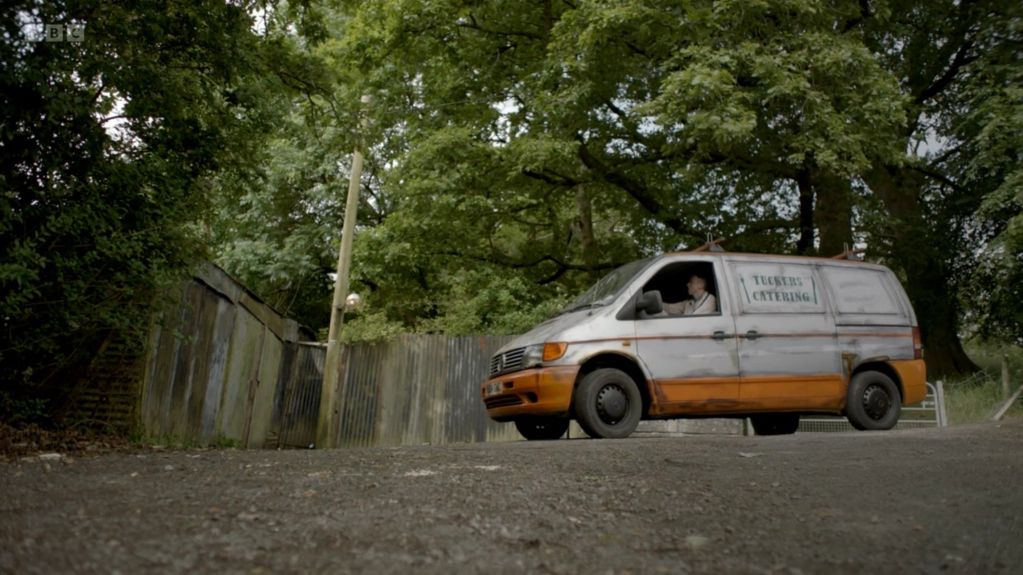 Rusty catering van parked on a gravel road surrounded by trees.