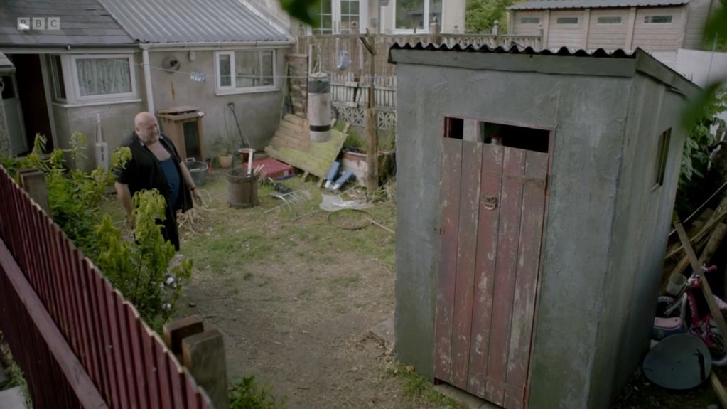 Man stands in a backyard near a shed.